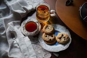 fotografie van een bord van koekjes en een glas van thee Aan een tafel met een kleding en een servet Aan het foto