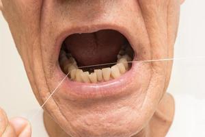 dichtbij omhoog van een ouder Mens flossen zijn tanden met tandheelkundig floss foto
