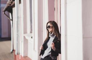 elegant meisje in zonnebril poseren Aan stad straat voorbijgaan foto