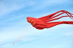 felrode roze octopusvlieger die in blauwe lucht vliegt met wolken, rode octopusvormige vlieger, vliegerfestival foto