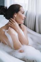 zelf liefhebbend volwassen glimlachen vrouw met brunette haar- nemen bad met schuim Bij huis foto