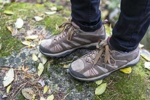 poten in vrouwen trekking sportschoenen Aan een bemost Woud steen met herfst geel bladeren, reizen concept, wandelen foto