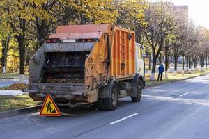 vuilnis vrachtauto verwijdert herfst gedaald bladeren, verwijdering van gedaald herfst bladeren door medewerkers van openbaar Gereedschap foto