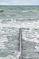 uitzicht op blauwe zee met schuimende golven en houten golfbrekers foto