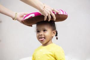 mama's handen zetten een grappig hoofdkussen Aan een weinig Afrikaanse meisje. foto