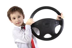 grappig weinig jongen is Holding een auto stuurinrichting wiel. jong bestuurder Aan een wit achtergrond. foto