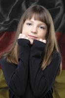 een mooi weinig meisje met een zoet glimlach, staand tegen de achtergrond van een wazig vlag van duitsland. foto