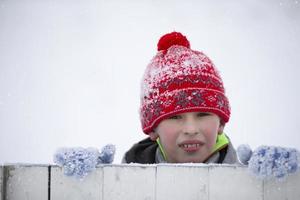 kind in winter. een weinig jongen in een warm hoed en wanten looks Bij de camera en glimlacht. foto