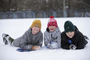 kinderen in winter. drie weinig jongen vrienden liggen in de sneeuw en kijken Bij de camera. foto