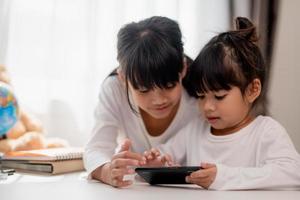 concept kinderen en gadgets. twee weinig meisjes broers en zussen zussen kijken Bij de telefoon en glimlach. ze houden een smartphone kijk maar videos, leren, Speel spellen, spreken online. internet voor kinderen. ouderlijk controle foto