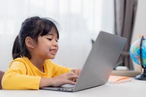 eerste dag Bij school. Aziatisch weinig meisje gebruik makend van een laptop computer, aan het studeren door online e-learning systeem. foto