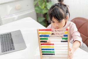 een jong schattig Aziatisch meisje gebruikt het telraam met gekleurde kralen om thuis te leren tellen foto