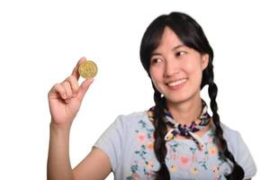 portret van mooi gelukkig jong Aziatisch vrouw in denim jurk Holding crypto valuta munt Aan wit achtergrond. foto