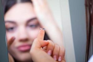 jong vrouw zetten contact lens in haar Rechtsaf oog, dichtbij omhoog foto