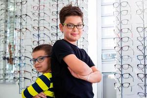 Gezondheid zorg, gezichtsvermogen en visie concept - twee jongens kiezen bril Bij optiek op te slaan foto