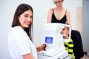 vrouw oogarts gebruik makend van machine voor controle oog zicht in kliniek. weinig jongen op zoek Bij uitrusting en dokter testen oog leerling in optisch op te slaan. concept van oog zorg en Gezondheid. foto