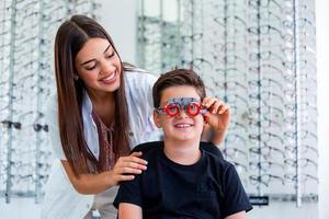 aantrekkelijk oogarts onderzoeken jong jongen met optometrist beproeving kader. kind geduldig naar controleren visie in oogheelkunde kliniek foto
