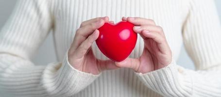 vrouw hand- Holding rood hart vorm geven aan. liefde, schenker, wereld hart dag, wereld Gezondheid dag en verzekering concepten foto