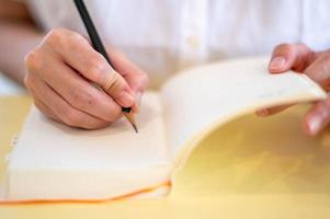 vrouw hand- maken Notitie met potlood en leeg notitieboekje in hun kamer. foto