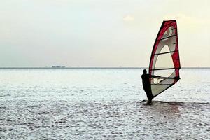 Mens windsurfer over- de zonsondergang foto