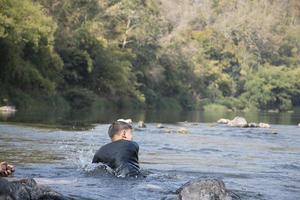 Aziatisch jongens zijn uitgeven hun vrije tijd door duiken, zwemmen, het werpen rotsen en vangen vis in de rivier- samen gelukkig. hobby en geluk van kinderen concept. foto