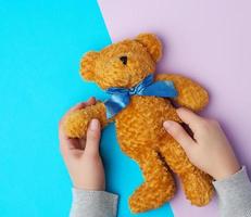 twee vrouw handen houden een klein bruin speelgoed- teddy beer Aan een blauw Purper achtergrond foto