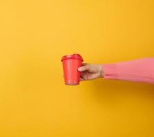 hand- houdt papier karton rood kop voor koffie, geel achtergrond. milieuvriendelijk serviesgoed foto