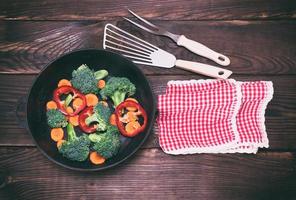 gietijzer frituren pan met stukken van wortels, broccoli foto