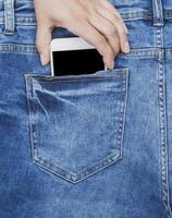 vrouw hand- trekt uit van de terug zak- van een blauw jeans smartphone foto