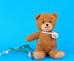 bruin teddy beer met een verbonden poot zittend Aan een blauw achtergrond foto
