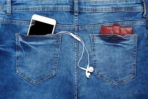 wit smartphone met hoofdtelefoons in de terug zak- van blauw jeans foto