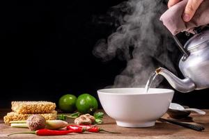 gieten heet water in een kom van ogenblik noedels of pasta. heerlijk heet soep Thais Chinese, Japans specerijen, citroen Chili shitake champignons geregeld Aan tafel geïsoleerd Aan zwart achtergrond. foto