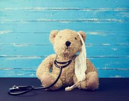teddy beer is zittend in een wit medisch masker, zwart stethoscoop is hangende Aan zijn nek foto
