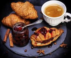 croissant met aardbei jam en wit kop met koffie foto
