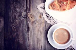 kop van koffie en een croissant Aan een schotel foto