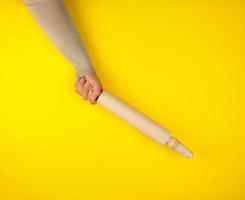 hand- Holding een houten rollend pin Aan een geel achtergrond foto