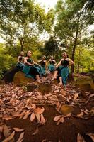 een groep van Aziatisch Dames duurt een vakantie naar de Woud terwijl vervelend een groen rok en zittend Aan een rots foto