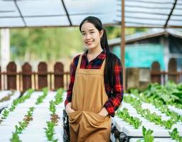 portret van gelukkig jong Aziatisch meisje boer op zoek Bij camera met vers groen eik sla salade, biologisch hydrocultuur groente in kinderkamer boerderij. bedrijf en biologisch hydrocultuur groente concept. foto