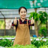 jong Aziatisch meisje boer tonen duim omhoog met vers groen eik sla salade, biologisch hydrocultuur groente in kinderkamer boerderij. bedrijf en biologisch hydrocultuur groente concept. foto