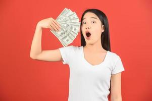 portret van een vrolijk jong vrouw Holding geld bankbiljetten en vieren geïsoleerd over- rood achtergrond foto
