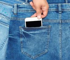vrouw hand- trekt uit van de terug zak- van een blauw jeans smartphone met een blanco scherm foto
