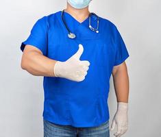 mannetje dokter in blauw uniform en latex wit handschoenen shows Rechtsaf hand- gebaar Leuk vinden foto