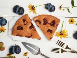 twee plakjes van biscuit Pruim taart Aan een wit houten bord en vers fruit foto