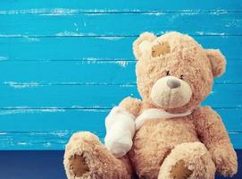 bruin teddy beer met teruggespoeld wit verband poot Aan een blauw houten achtergrond foto