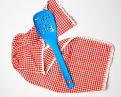 blauw plastic keuken lepel leugens Aan een rood Wit keuken handdoek foto