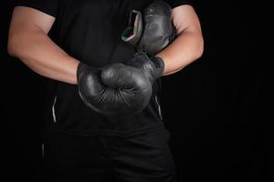 volwassen gespierd Mens in zwart kleren zet Aan leer zwart boksen handschoenen foto