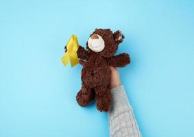 klein bruin teddy beer welke houdt in haar poot een geel lint gevouwen in een lus foto
