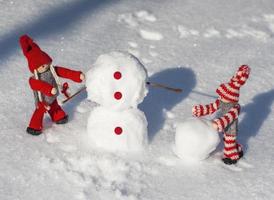 houten poppen in rood gebreid kleren rollen naar beneden sneeuwballen naar bouwen een sneeuwman foto