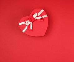geschenk doos in de het formulier van een hart met een boog Aan een rood achtergrond foto