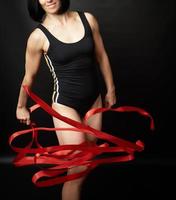 jong vrouw gymnast van Kaukasisch uiterlijk met zwart haar- spins rood satijn linten, gymnastiek- opdrachten foto